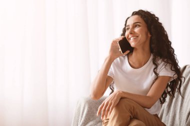 Uzun kıvırcık saçlı mutlu esmer bayan pencerenin önünde oturmuş arkadaşlarıyla ya da sevgilileriyle neşeli bir şekilde konuşuyor. İzolasyon sırasında iletişim
