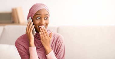 Modern iletişim konsepti. Evde cep telefonuyla konuşan tesettürlü Müslüman bir kadının arkadaşıyla sohbet etmesine şaşırdım. Türbanlı güzel Arap bayan, dedikodu yapıyor, şok edici haberleri tartışıyor.