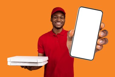 Hızlı Pizza Teslimatı. Kırmızı şapkalı ve üniformalı gülümseyen Afro-Amerikan erkek kuryenin portresi restorandan pizza kutusunu tutuyor ve turuncu sarı stüdyo arka planında izole edilmiş saati gösteriyor.