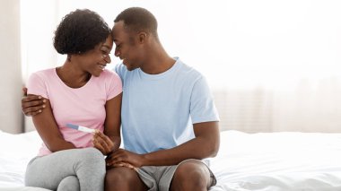 Genç siyah çift ebeveyn olacak, pozitif hamilelik testi yapacaklar ve birbirlerine alınlarıyla dokunacaklar, yatak odasının içi boş olacak. Memnuniyetle Afro-Amerikan ailesi bebek bekliyor.