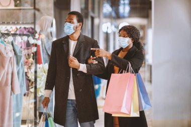 Kara Cuma ve Covid-19 karantina. Binlerce yıllık Afro-Amerikan erkek ve kadın paltolu ve tıbbi maskeli, ellerinde paketlerle alışveriş yaptıktan sonra, alışveriş merkezlerinde büyük indirimler, bedava uzay boşlukları...