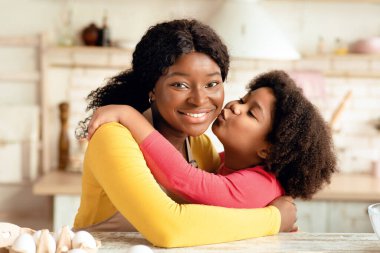 Anneler Günün kutlu olsun. Sevimli küçük siyah kız mutfakta birlikte yemek pişirirken annesini öpüyor ve kucaklıyor Afrikalı çocuğu seviyor ve annesiyle vakit geçiriyor.