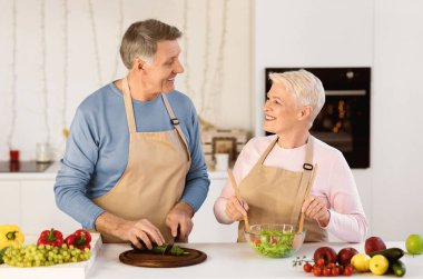 Cheerful Aged Couple Cooking Salad Preparing Dinner In Modern Kitchen At Home. Senior Spouses Enjoying Food Preparation Together. Healthy Nutrition Recipes, Dieting In Older Age Concept
