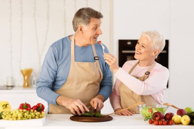 Yaşlanmış eşler yemek pişiriyor ve yemek tadıyor yemek hazırlarken evde modern mutfakta durup eğleniyorlar. Son sınıf aile yemeği hazırlayan hafta sonunun tadını çıkarıyorlar..