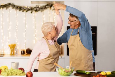 Olgun evli çift mutfakta dans ediyor, Noel arifesinde birlikte yemek pişiriyor. Kıdemli eşler evde yeni yıl yemeği hazırlıklarının keyfini çıkarıyorlar. Aile Kış Tatillerinde Evde Yemek Pişirir