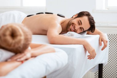 Çift Sıcak Taş Masajı. Mutlu koca, karısına gülümseyen, romantik balayı boyunca masaj terapisinde yalan söyleyen ve rahatlatan. Güzellik, rahatlık ve sağlık. Seçici Odaklanma