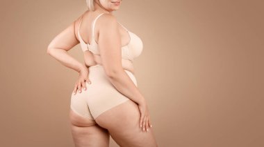 Kahverengi stüdyo arka planında bej iç çamaşırlı genç bir kadın, yarım dönük kamera, kırpılmış boş alan görüntüsü.