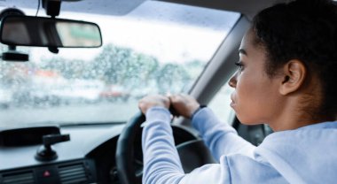 Yağmurlu havalarda ve işe giderken şehirde taksi şoförü olarak çalışmak. Odaklanmış genç Afrikalı Amerikalı kadın araba kullanıyor ve direksiyonu tutuyor, yol kenarına yağmur damlalarıyla bakıyor, boş bir alan.