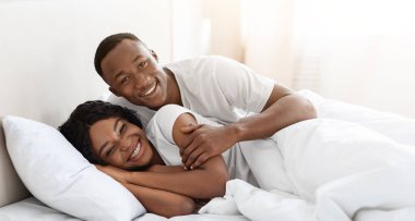 Mutlu Afro-Amerikalı çift evde yatakta kaynaşıyor, aşkta birlikte olmanın ve şefkatin tadını çıkarıyorlar, kopyalama alanında. Neşeli zenci aile babası ve aşık kadın yatak odasında eğleniyorlar.