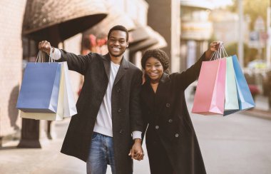 Kara Cuma ve satış sezonu boyunca düşük fiyata harika alışveriş. Mutlu, genç, Afro-Amerikan karı-koca paltolu birçok renkli alışveriş torbası gösteriyor cadde, alışveriş merkezi yakınında, fotokopi alanı