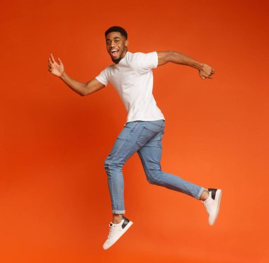 Turuncu studio arka planda, kameraya gülümseyen atlama havada, yürüyüş neşeli bin yıllık Afrikalı-Amerikalı adam