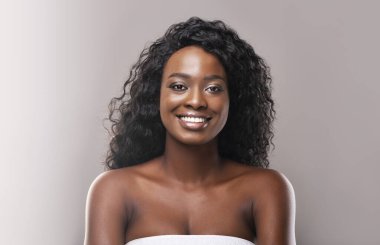 Gri stüdyo arka planında kusursuz derisi olan güzel, gülümseyen Afro-Amerikan kadının portresi.