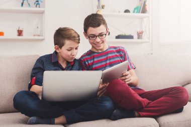 Teknoloji, çocuk dostluk ve iletişim kavramı - iki sevimli gençler evde oturma odasında kanepede otururken tablet ve dizüstü bilgisayar kullanarak