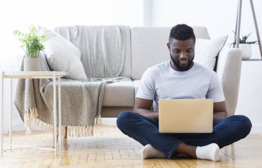 Merkez ofis. Siyah serbest yazar dizüstü bilgisayarda, oturma odasında yerde oturuyor, boş yer var.