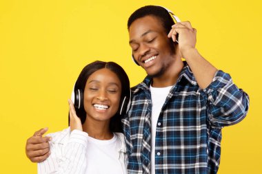 Birlikte en sevdiğiniz müzik ve covid-19 'da kalın. Kablosuz kulaklıklı, gülümseyen Afro-Amerikan çift boş zamanlarında şarkıdan zevk alıyor, sarı arka planda izole edilmiş, stüdyo çekimi, kopyalama alanı