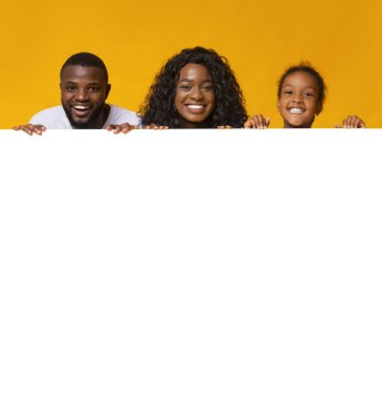 Aile teklifi. Siyah ebeveynler ve kızları reklam için boş beyaz tahtaya yaslanıyorlar.