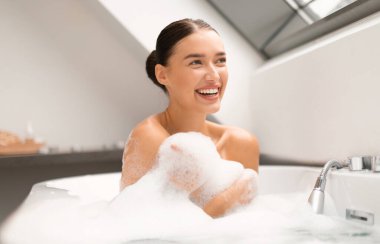 Küvette köpükle kaplanmış, evde banyo yapan, yan yan bakıp gülümseyen neşeli kadın cesedi. Banyo 'da banyo yapan bir kadın. Güzellik ve Refah Konsepti