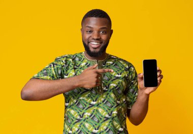 Mutlu Afro-Amerikan adam boş akıllı telefon ekranını işaret ediyor, yeni bir uygulama öneriyor, sarı arka plan