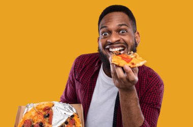 Stüdyoda aşırı yemek yeme pozuna gülümseyen pizza yiyen komik siyahi adamın portresi. Erkek Foodie Junk Food 'un tadını çıkarıyor. Sağlıksız Beslenme ve Aldatma Yemekleri