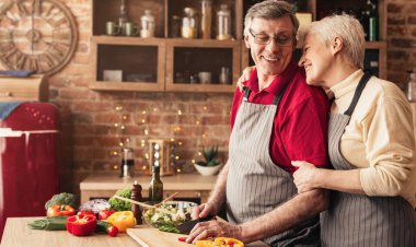 Aşk ve ev hayatı. Neşeli son sınıf kadını mutfakta kocasına sarılıyor, panoramada boş yer var.