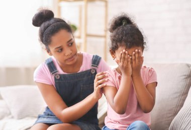 Kardeş ilişkileri ve destek kavramı. Afrikalı genç kız ağlayan kız kardeşini kucaklıyor, özür diliyor ya da evde teselli ediyor.