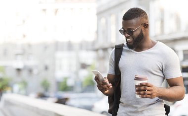 İşe giderken. Neşeli sakallı Afrikalı adam akıllı telefon kullanarak ve kahve içme, panorama, boş alan