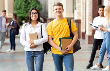 Üniversite kampüsünde kameraya gülümseyen mutlu öğrenciler.