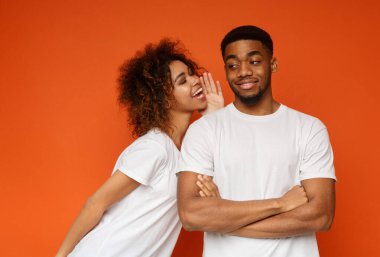 Bana sırlarını söyle. Hoş gülümseyen Afrikalı-Amerikalı kadın erkeğini önemli bir şey için kulak fısıldayan turuncu arka plan