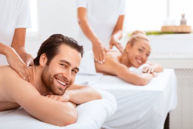 Spa Salonu 'nda sırt masajı alan mutlu çift. Eşler, evdeki yataklarda uzanan kameraya gülümseyen birlikte güzellik tedavisinden hoşlanırlar. Balayı Tatil Gevşemesi, Romantik Sağlık Prosedürü