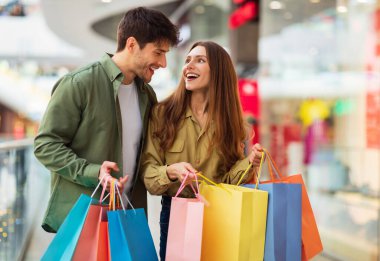 Alışveriş yaparken neşeli bir çift. Renkli alışveriş torbaları. Hafta sonları modern hipermarketten yeni kıyafetler alıyorlar. Hafta sonunu alışveriş merkezinde geçiren mutlu müşteriler. Büyük Satış Konsepti