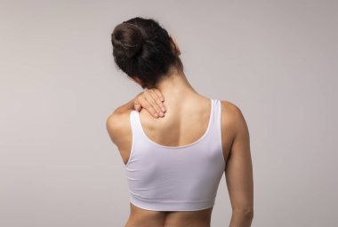 Boyun ve sırt ağrısı olan, boynu ağrıyan esmer bir kadın ofis sendromundan muzdarip bir kadın, arka plan, gri stüdyo arka plan, fotokopi odası.