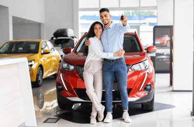 Mutlu, güzel, Müslüman bir aile babası genç bir adam ve uzun saçlı bir kadın salonda yeni bir araba satın alıyor, kırmızı lüks otomobilin başında duruyor, yeni arabalarının anahtarlarını gösteriyor ve sarılıyorlar.