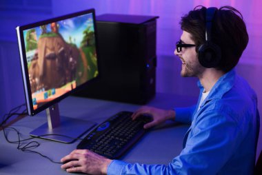Erkek oyuncu bilgisayarda nişancı oyunu oynuyor, kulaklık ve gözlük takıyor.