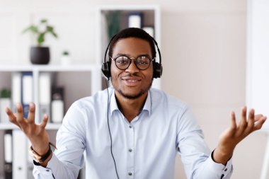 Kulaklıklı, el kol hareketleriyle konuşan, gözlüklü, ofis içi, fotokopi odası olan Afro-Amerikan bir adamın portresi. Pozitif siyah hoparlör çevrimiçi konferans yapıyor, iş yerinden video görüşmesi yapıyor.
