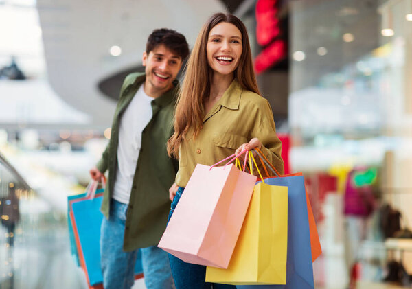 Веселая пара ходить по магазинам и носить красочные сумки, весело во время больших сезонных продаж Покупка новой одежды вместе в современном торговом центре. Покупатели проводят выходные в гипермаркете