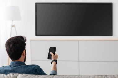 Genç adam boş ekranlı televizyon izliyor ve akıllı telefondan akıllı televizyon uzaktan kumandası kullanıyor. Menüden film akışını seçin, kanal veya ayarları değiştirin