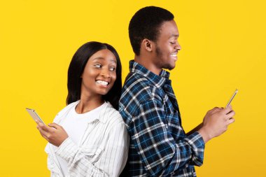Bloglar, sosyal medya, sıradışı mesaj ve ilginç olay. Neşeli, Afro-Amerikalı genç bir bayan gülümseyen kocanın akıllı telefonuyla omzunun üzerinden bakıyor, sarı arka planda izole edilmiş, stüdyo çekimi.