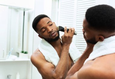 Çalışmaya hazırlanıyorum. Genç siyahi adam sakalını banyoda budayarak düzeltiyor.