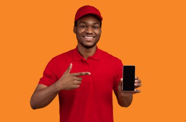 Teslimat Servisimizi Seç. Gülümseyen Afro-Amerikan kuryesi elinde cep telefonuyla elinde boş ekranla kırmızı başlık takıyor ve üniformasını giyiyor. Siyah, boş bir alete bakıyor.