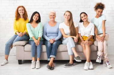 Farklı yaşlardaki mutiryaki kadınlar koltuğa oturup içeride birlikte gülümsüyorlar. Kadın Desteği ve Eşitlik