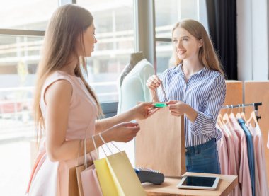 Gülümseyen beyaz kadın asistan giyim showroom müşteriye alışveriş yapıyor, kredi kartı ile ödeme