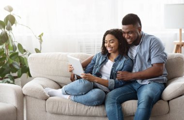 Karantina Eğlence Konsepti. Mutlu siyah çift evde dijital tabletle rahatlıyor, birlikte videolar izliyor ya da internette geziniyor.