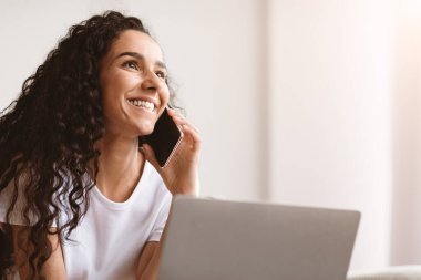 Cep telefonuyla konuşan, fotokopi odasına bakan, dizüstü bilgisayar kullanan mutlu bir bayanın yakın çekimi. Neşeli kıvırcık kadın evde çalışıyor, iş arkadaşlarıyla ya da müşterileriyle telefonda konuşuyor.