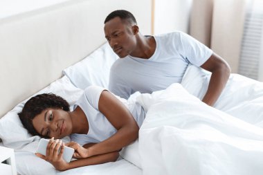 Kafası karışmış siyah bir adam, gülümseyen karısını cep telefonuyla gözetliyor, akıllı telefon ekranına bakıyor. Afro-Amerikalı genç bir çift yatakta uzanıyor, mutlu bir kadın birileriyle sohbet ediyor. Aileye güvensizlik