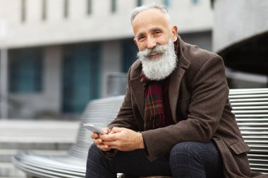 Gülümseyen gri saçlı, cep telefonlu, caddede bankta oturan, kameraya gülümseyen, kopyalayan yaşlı bir adam. Uzun sakallı yakışıklı bir adam ofis binasında dinleniyor, iş yerinde öğle yemeği yiyor.