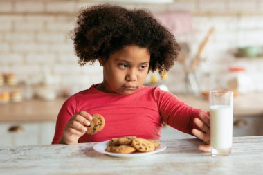 Huysuz küçük siyah kız mutfakta süt içip kurabiye yemeyi reddediyor, Afrikalı bayan çocuk sağlıklı kalsiyum içeceği yerine taze çikolatalı bisküvi seçiyor,
