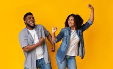 Dans Eğlencesi. Neşeli Afrikalı Amerikalı çift, birlikte takılıyor, dans ediyor ve gülüyor, sarı arka planda boş alanla poz veriyorlar.