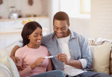 Ebeveynlik ve çocuk doğurma kavramı. Pozitif hamilelik testi olan mutlu siyahi anne-babalar yeni bir hayat için heyecanlı bebek bekliyorlar. Neşeli Afrikalı Amerikalı çift iyi haberler öğreniyor