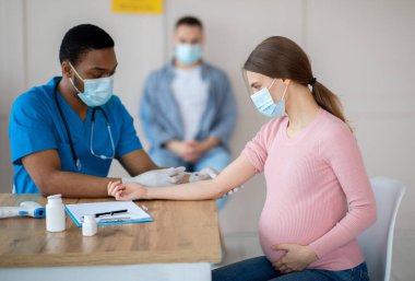 Afro-Amerikalı doktor Covid-19 aşısını sağlık merkezindeki genç hamile kadına enjekte ediyor. Muhtemel kadın klinikte koronavirüse karşı bağışıklık kazanıyor. Nüfus aşılama kavramı