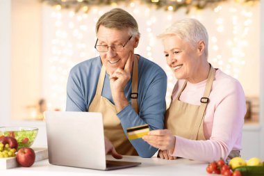 Market Noel Teklifi. Laptoplu ve kredi kartlı mutlu son sınıf çifti modern mutfaktan yemek alıyor. Yaşlı eşler internet bankacılığı aracılığıyla sipariş ve ödeme yapıyor.